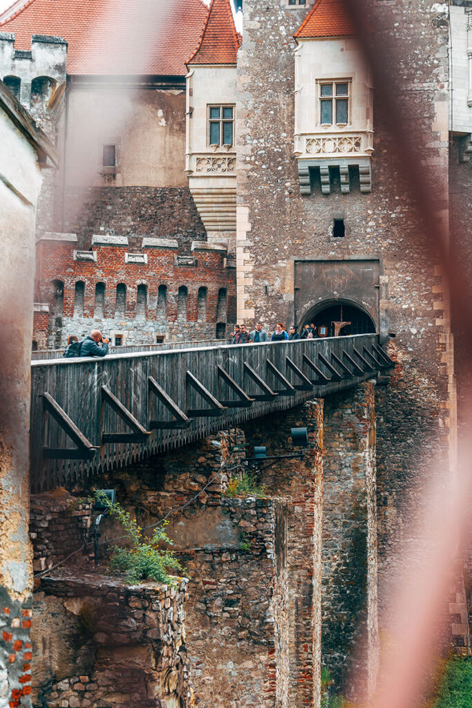 människor på en träbro som leder in till ett slott